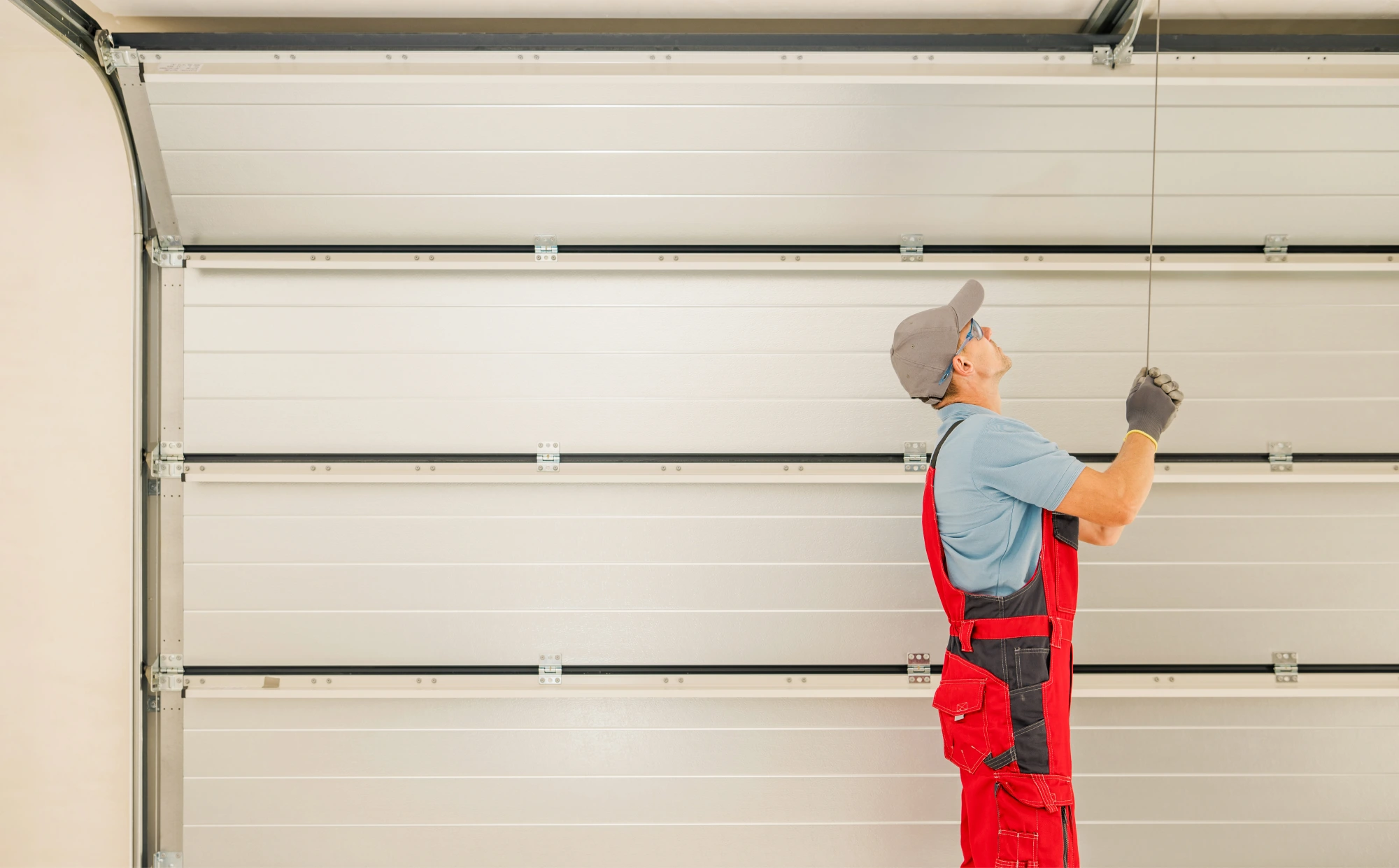 Man in red overalls and grey cap installing a garage door.