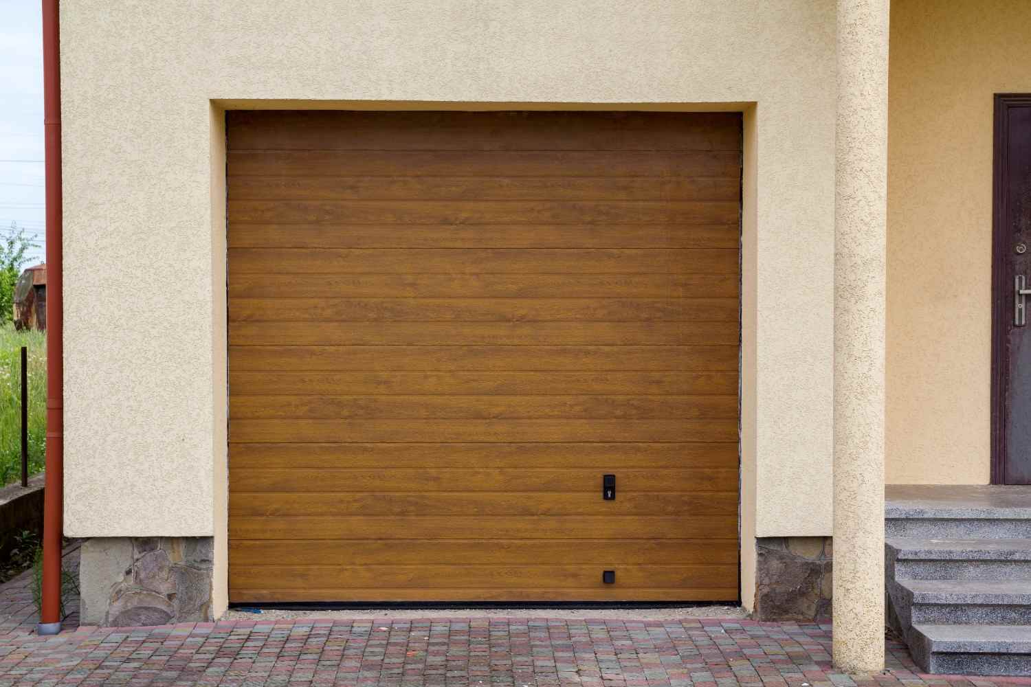 Brown garage door on a beige stucco house with stone trim.