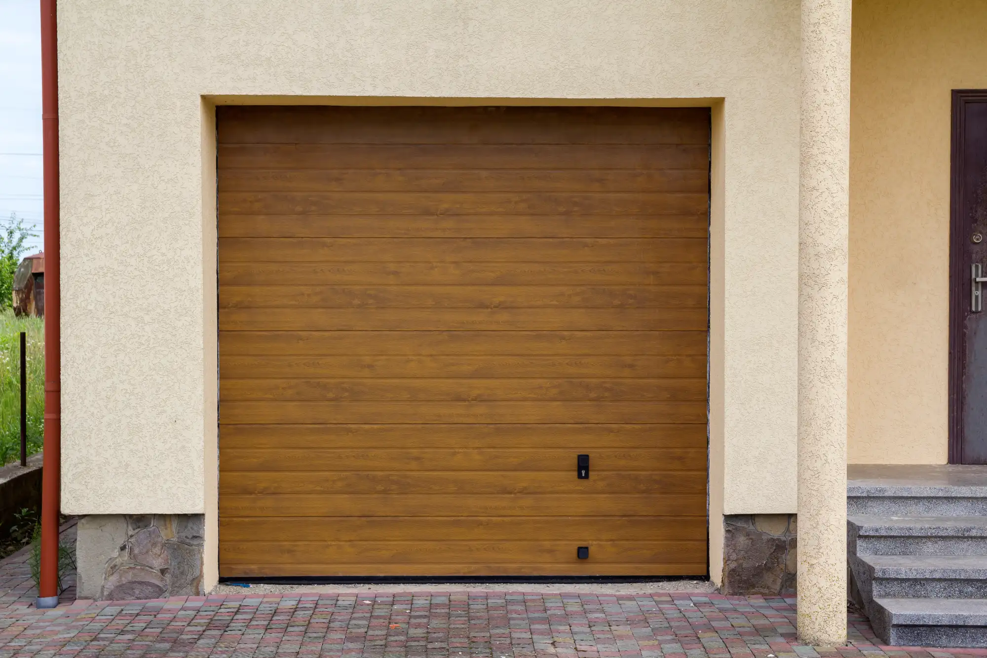 Closed brown garage door on a beige house with stone foundation.