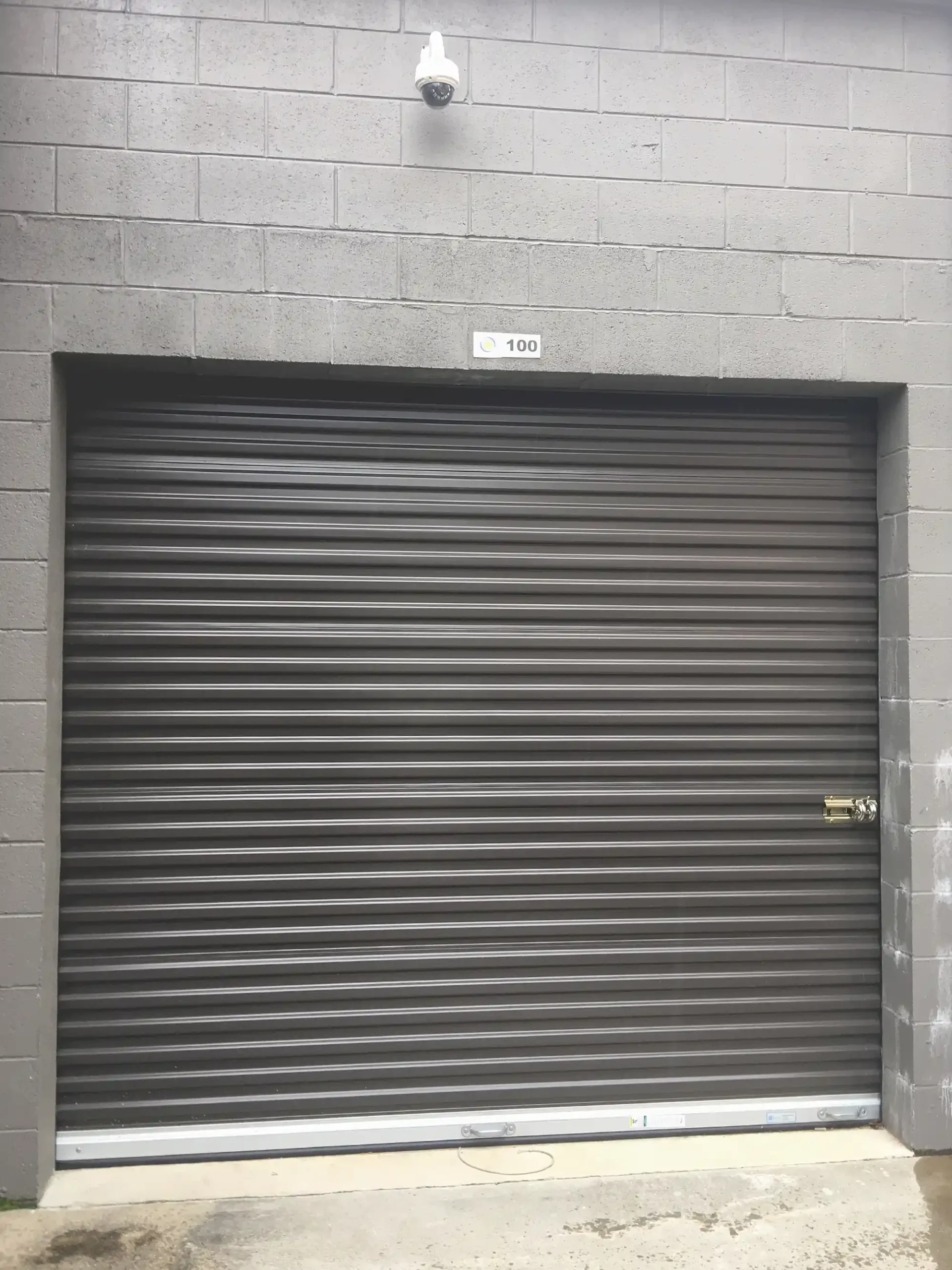 Brown roll-up storage unit door with a security camera above it