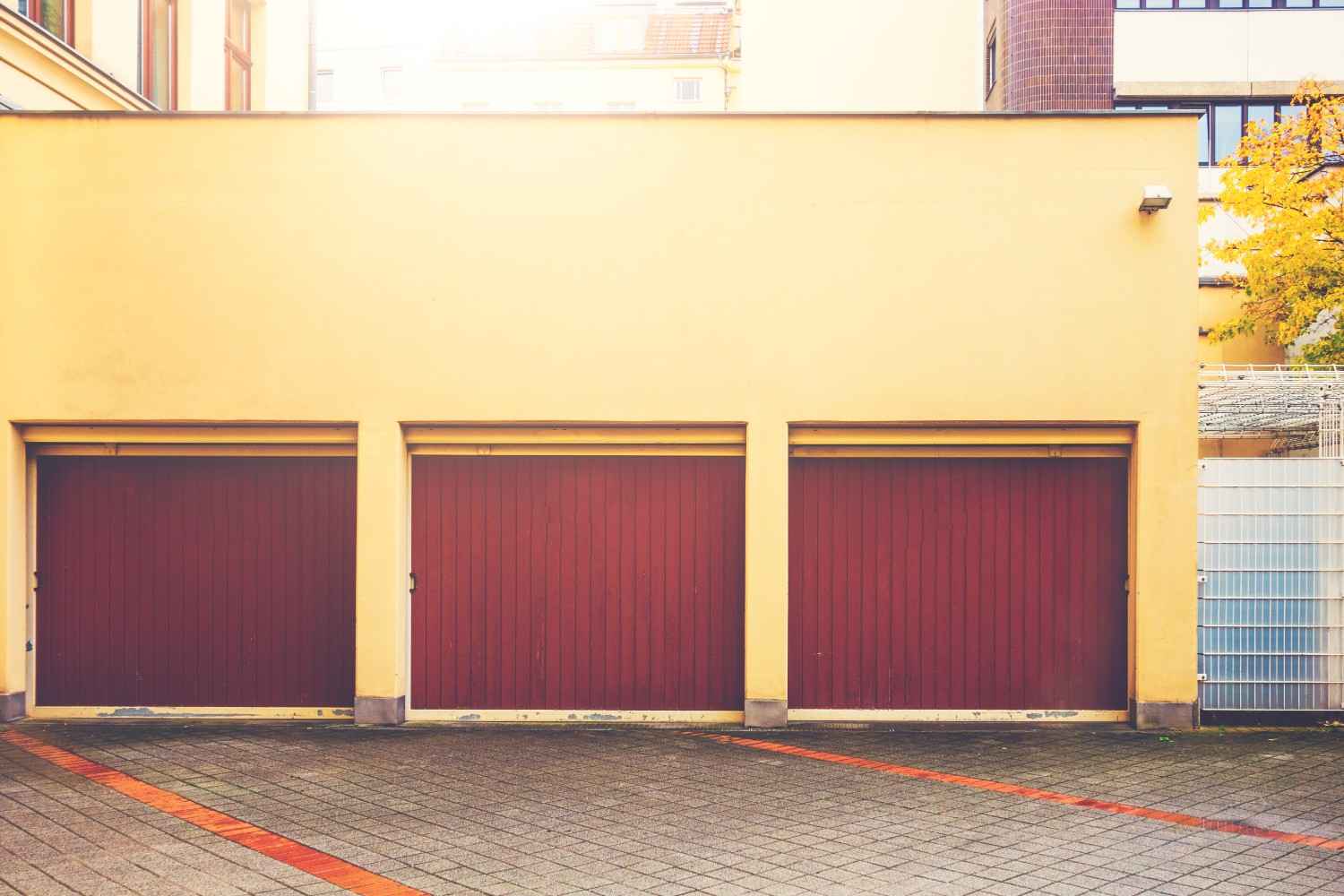 Three red garage doors on a yellow building with a paved driveway.