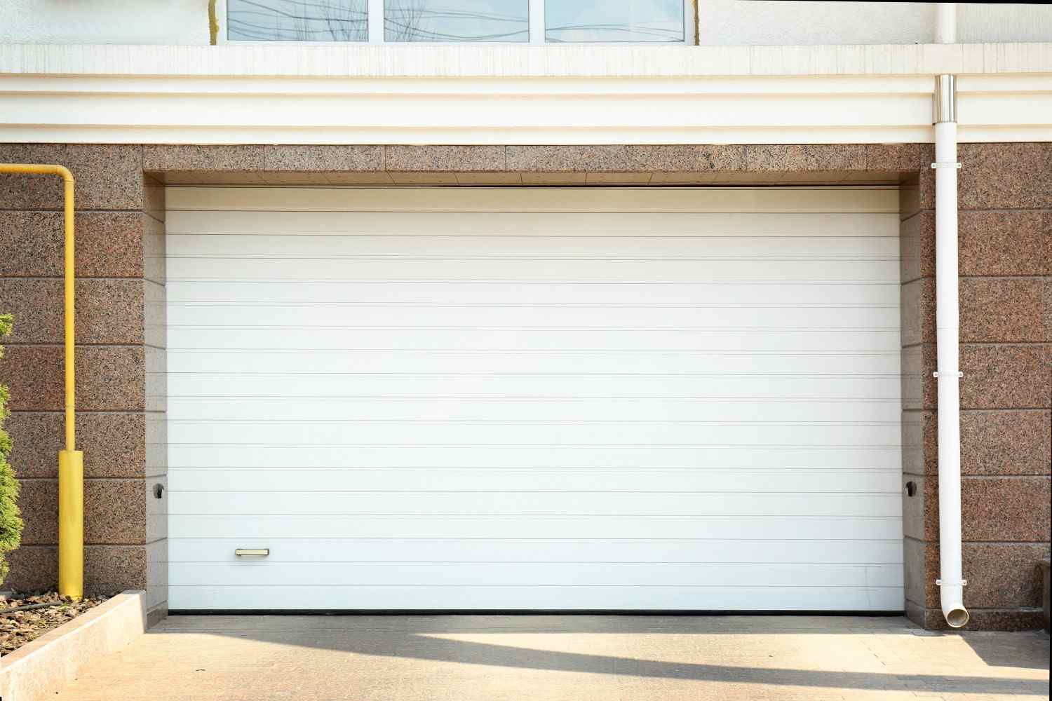 White garage door on a stone and concrete building with a yellow pipe