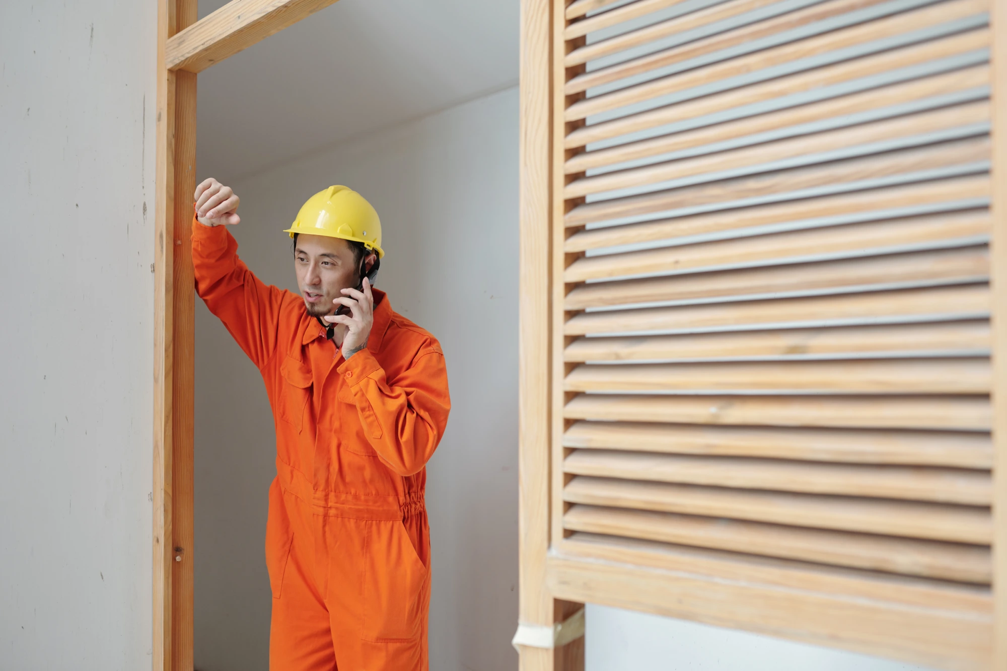 Man in orange jumpsuit and yellow hard hat talking on phone