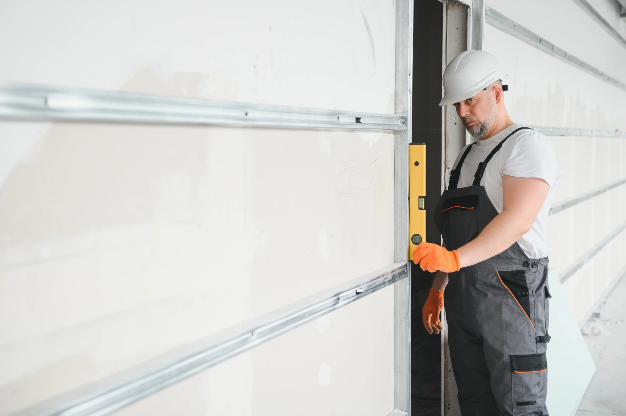 Man in hard hat and overalls using a level on a wall
