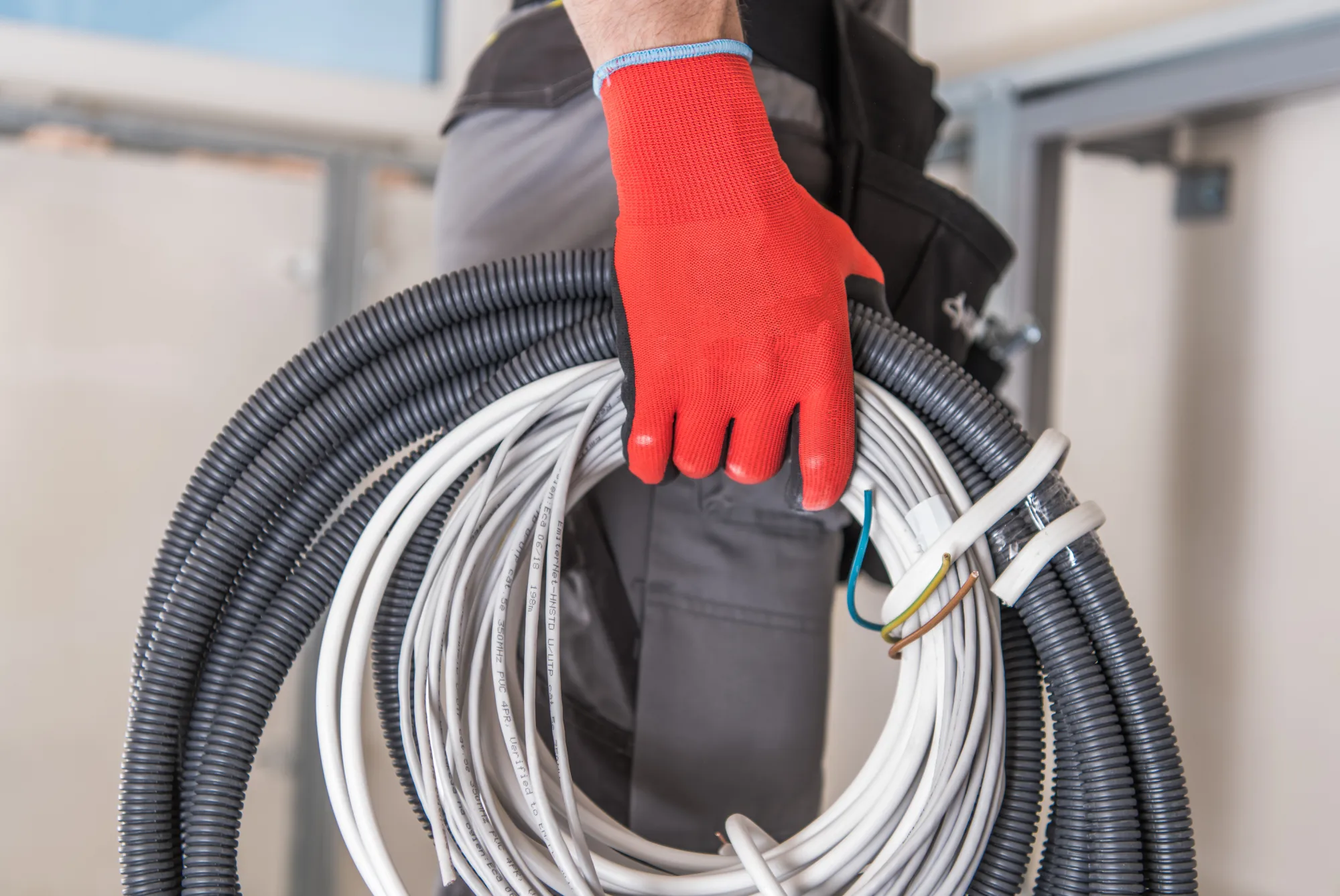 Man in red glove holding coiled electrical conduits and white wires.