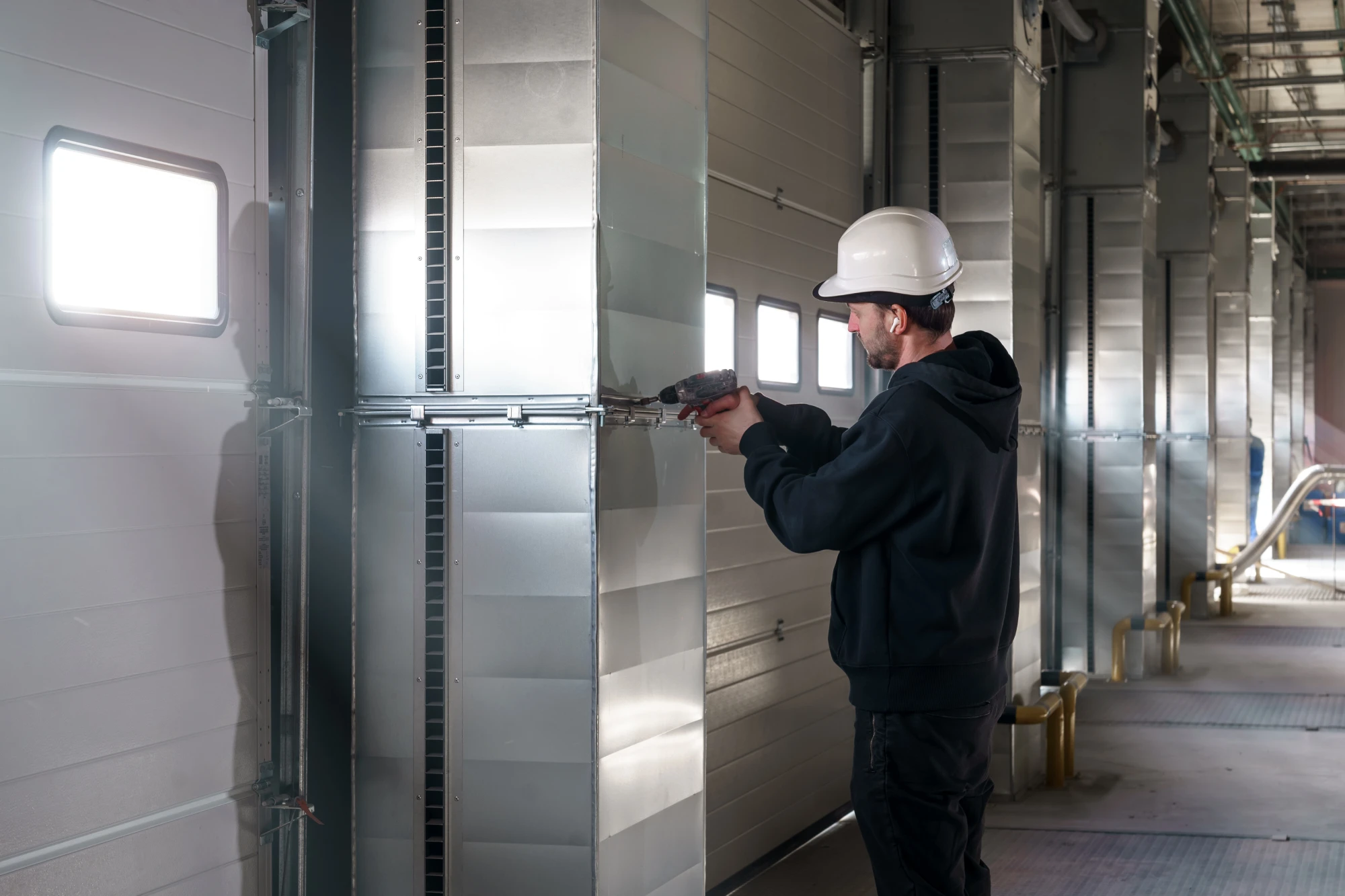 Man in hard hat drilling into metal ductwork in industrial setting