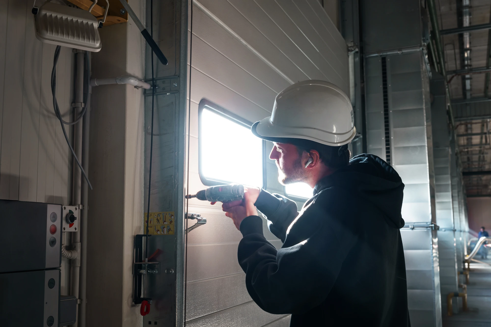 Man in hard hat using a drill on a garage door.