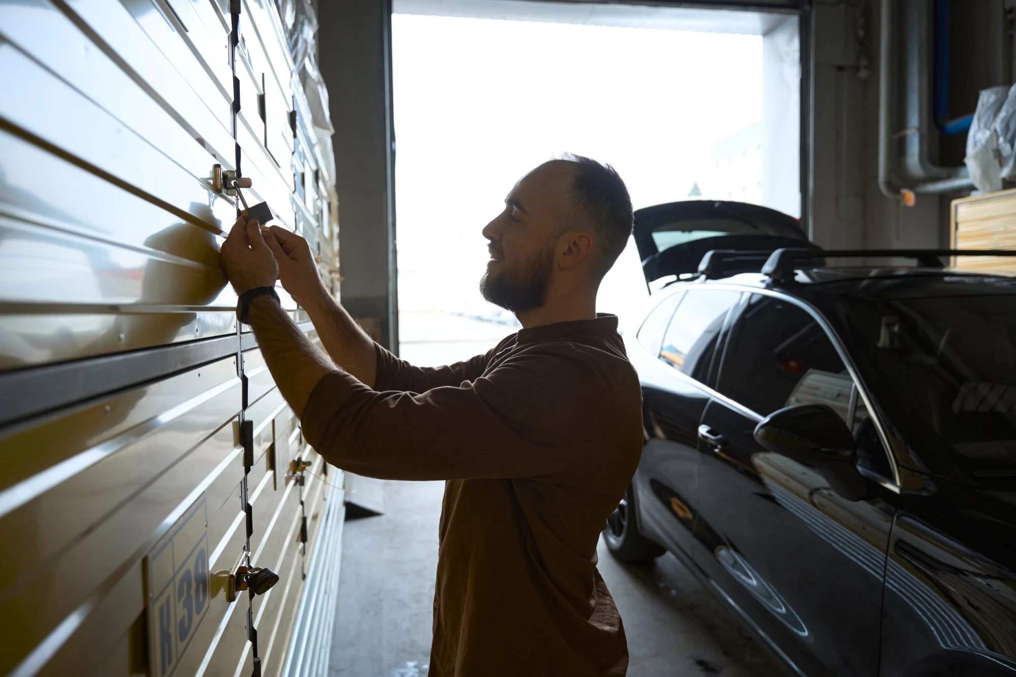 Man opening a storage unit with a key, a black car in the background