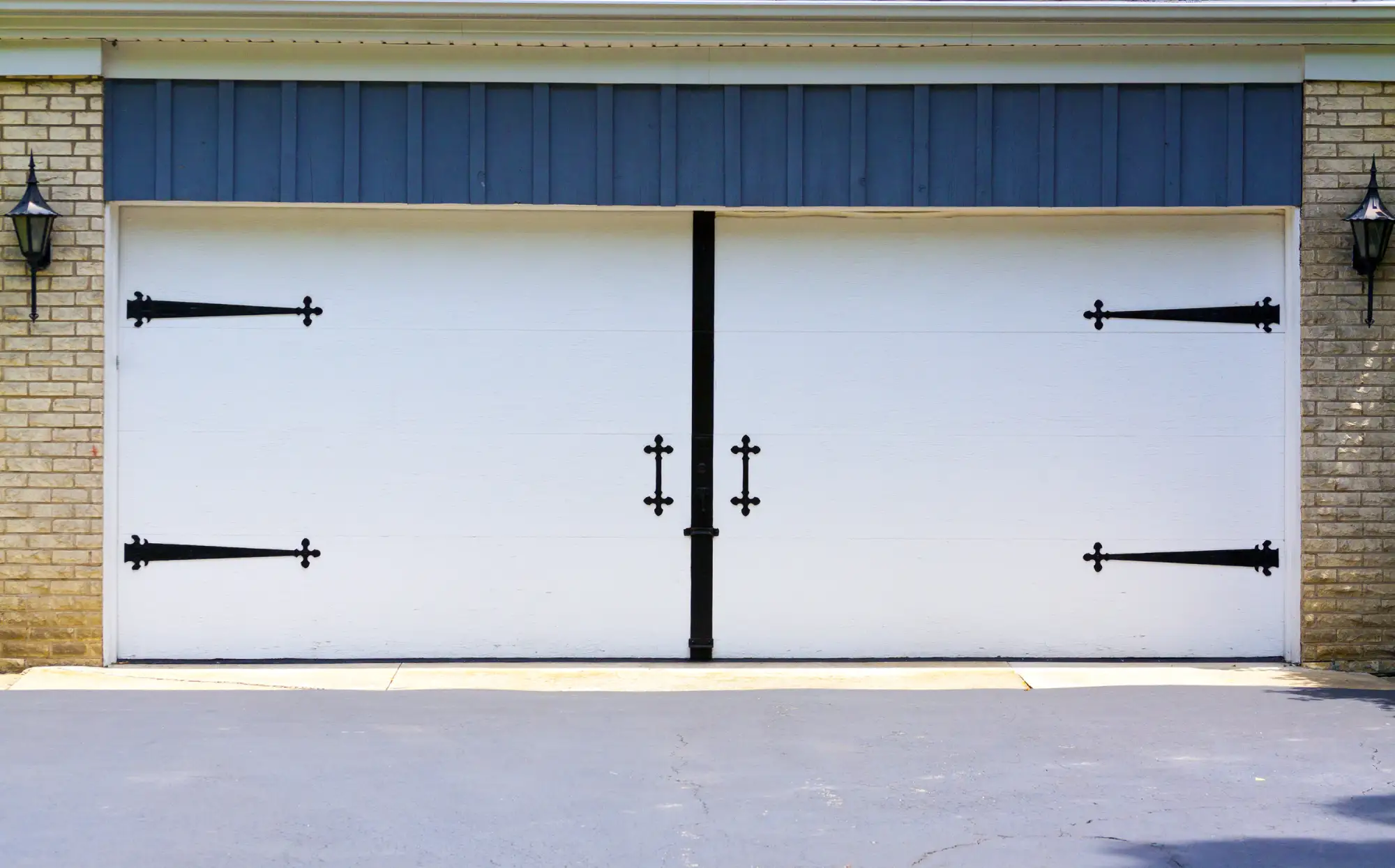 White garage door with decorative black hardware and brick facade