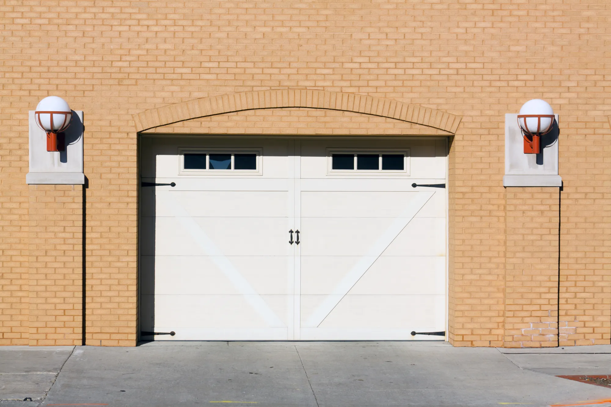 White garage door with windows and two spherical lights on a brick wall.