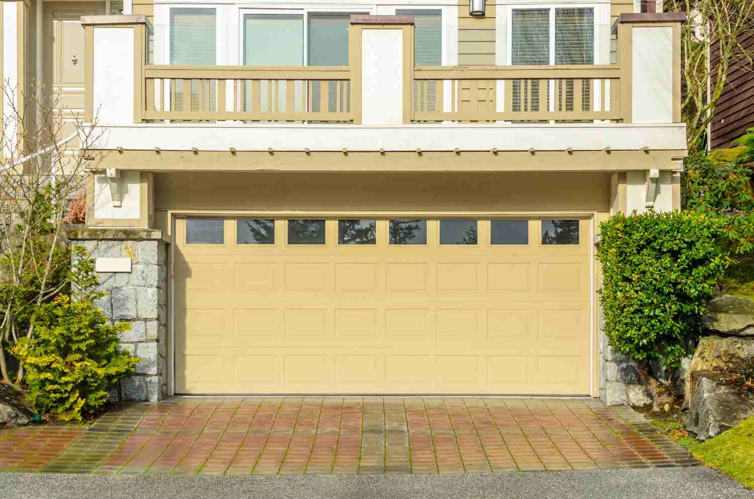 Beige garage door with windows and a brick driveway.