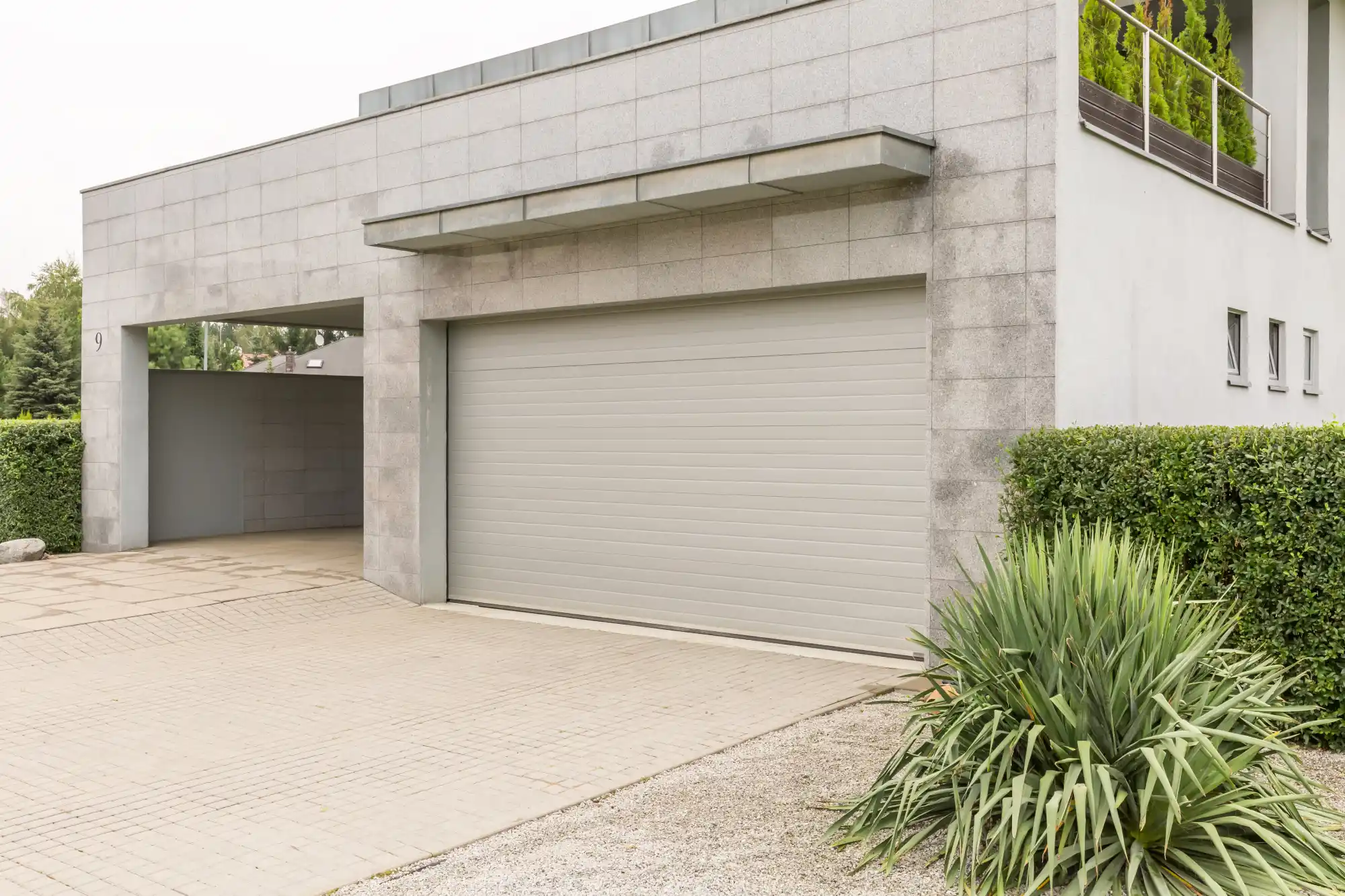Modern house exterior with two garage doors and lush green landscaping.