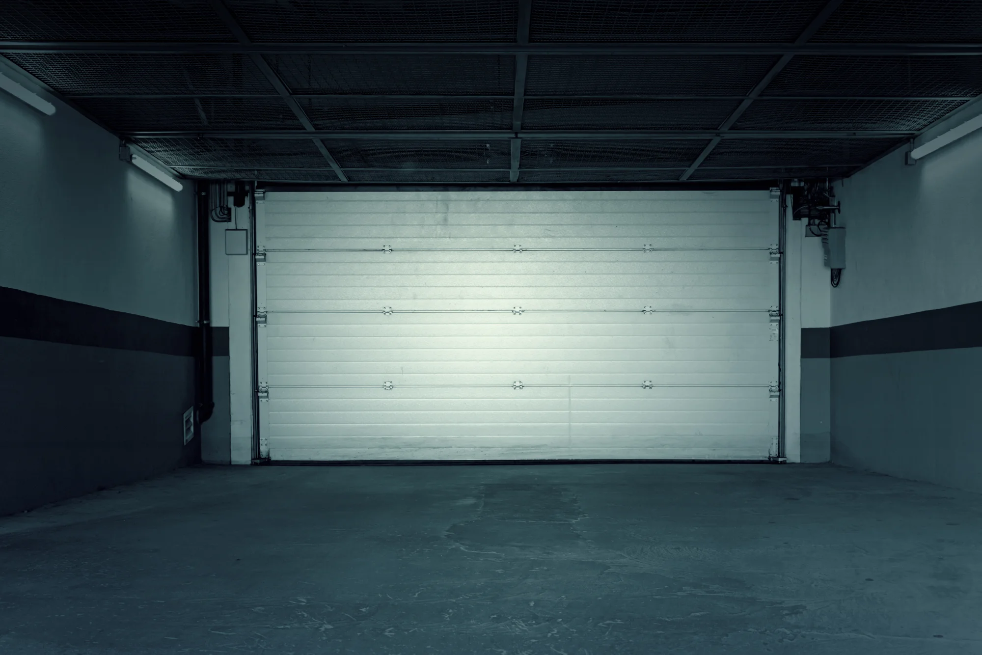 Closed white garage door in a dimly lit underground parking lot.