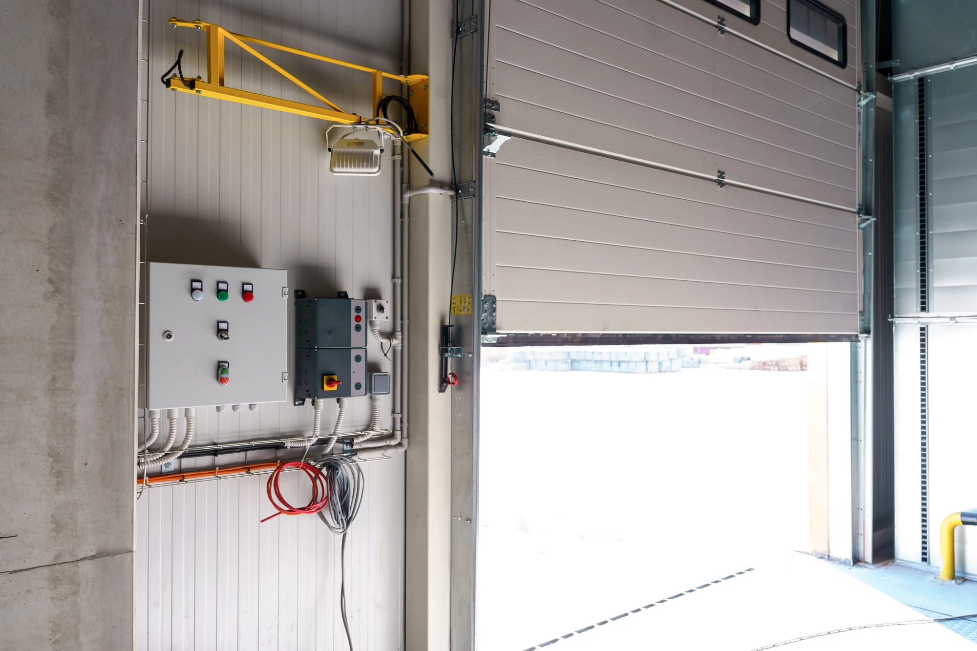 Partially open industrial garage door with control panels and wiring