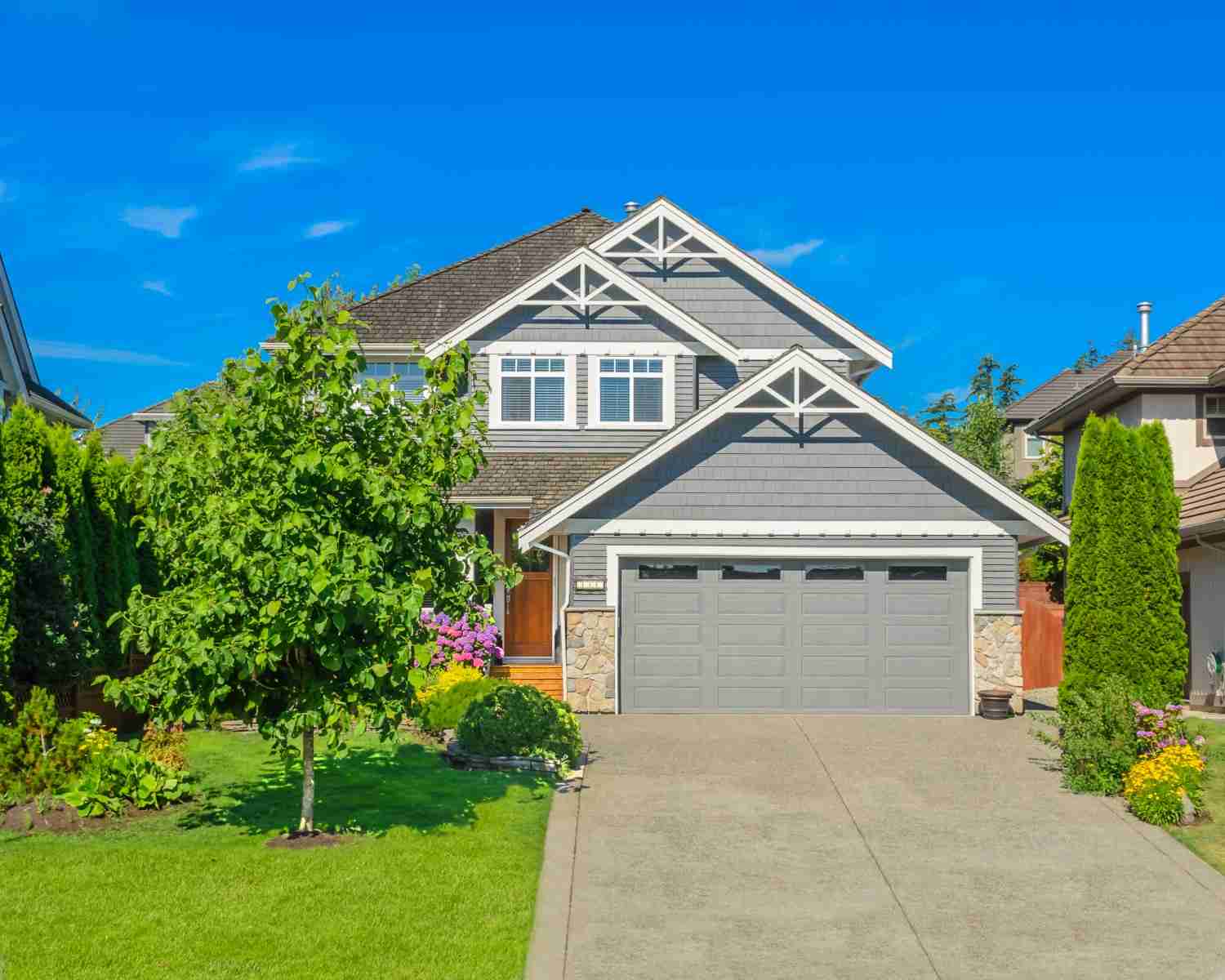 Grey house with stone accents, a two-car garage, and green landscaping.