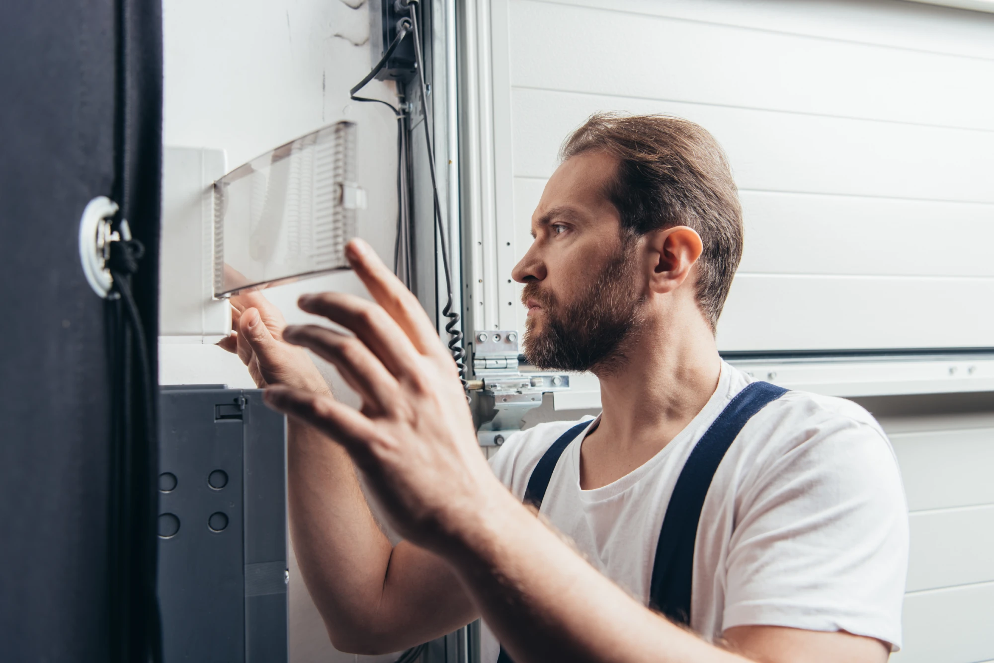 Man in white t-shirt and overalls working on a garage door mechanism