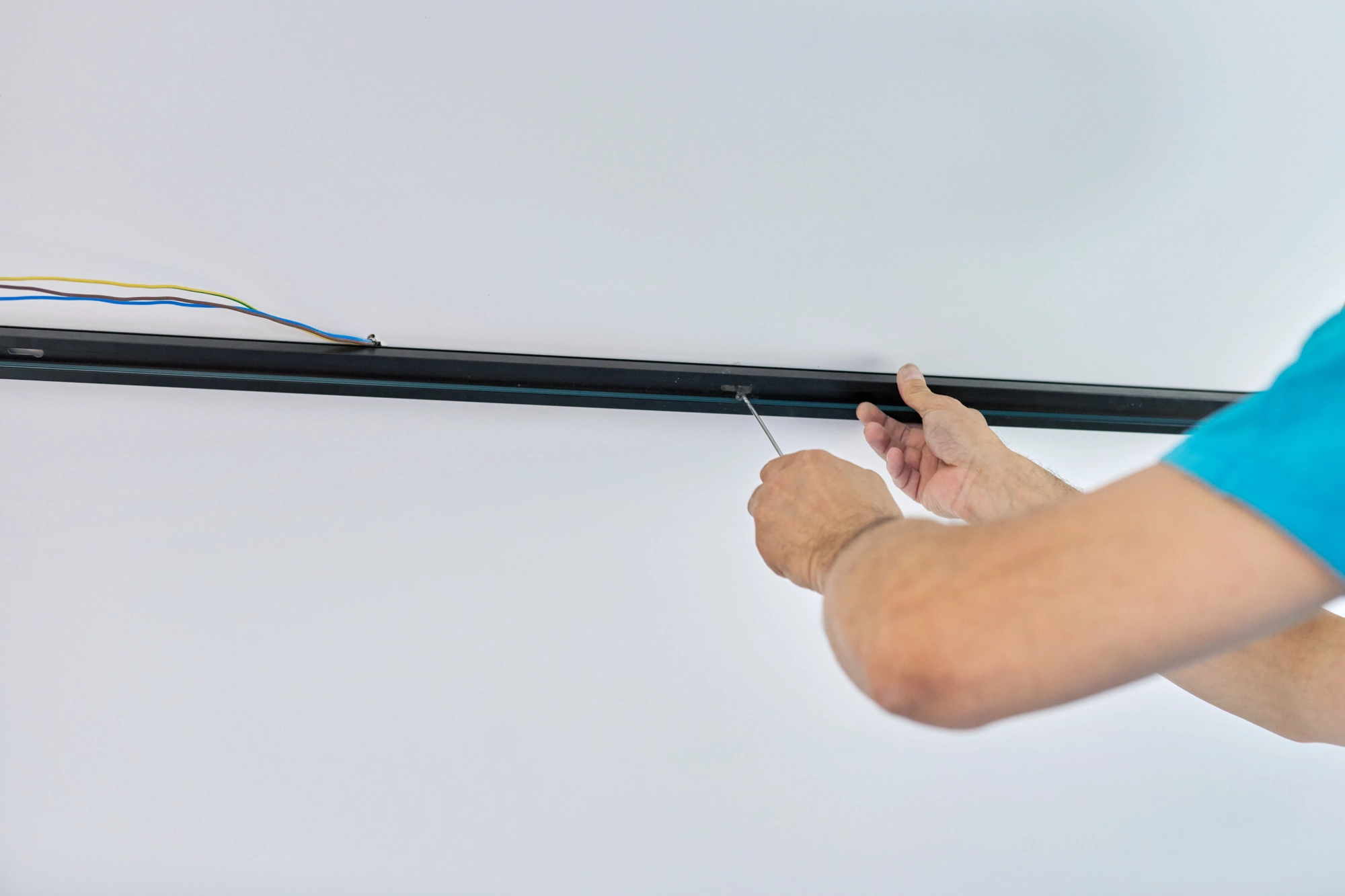 Man's hands installing a black track light rail on a white ceiling.