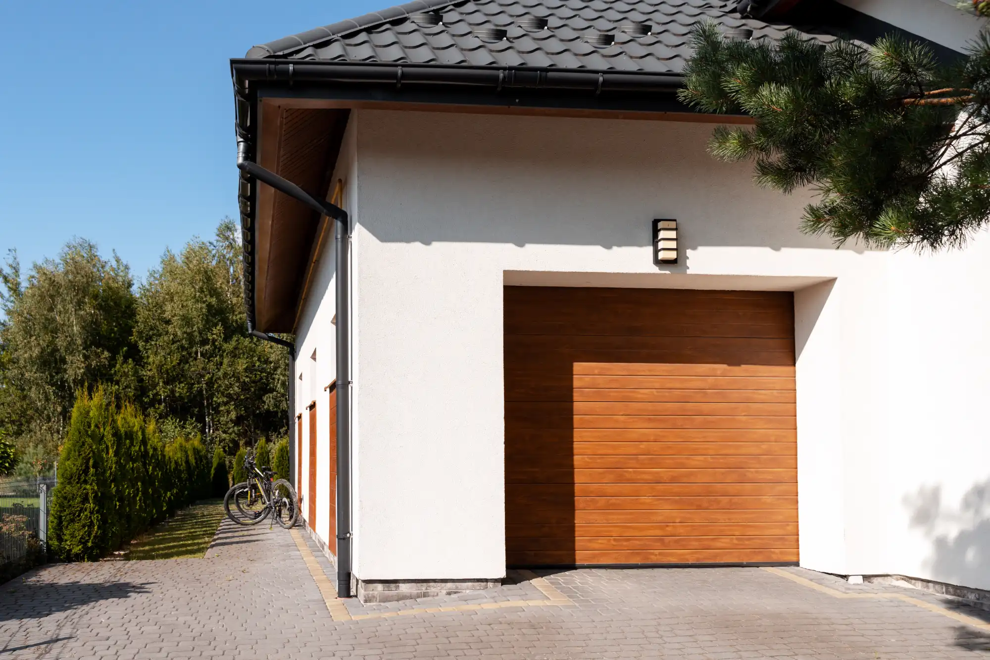 Modern white house with a wooden garage door and dark roof tiles.
