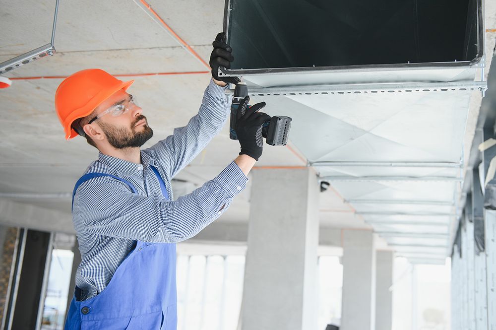 Man in orange hard hat installing ventilation system with a drill
