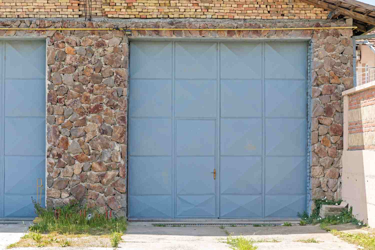 Two large blue metal garage doors set in a stone and brick building.