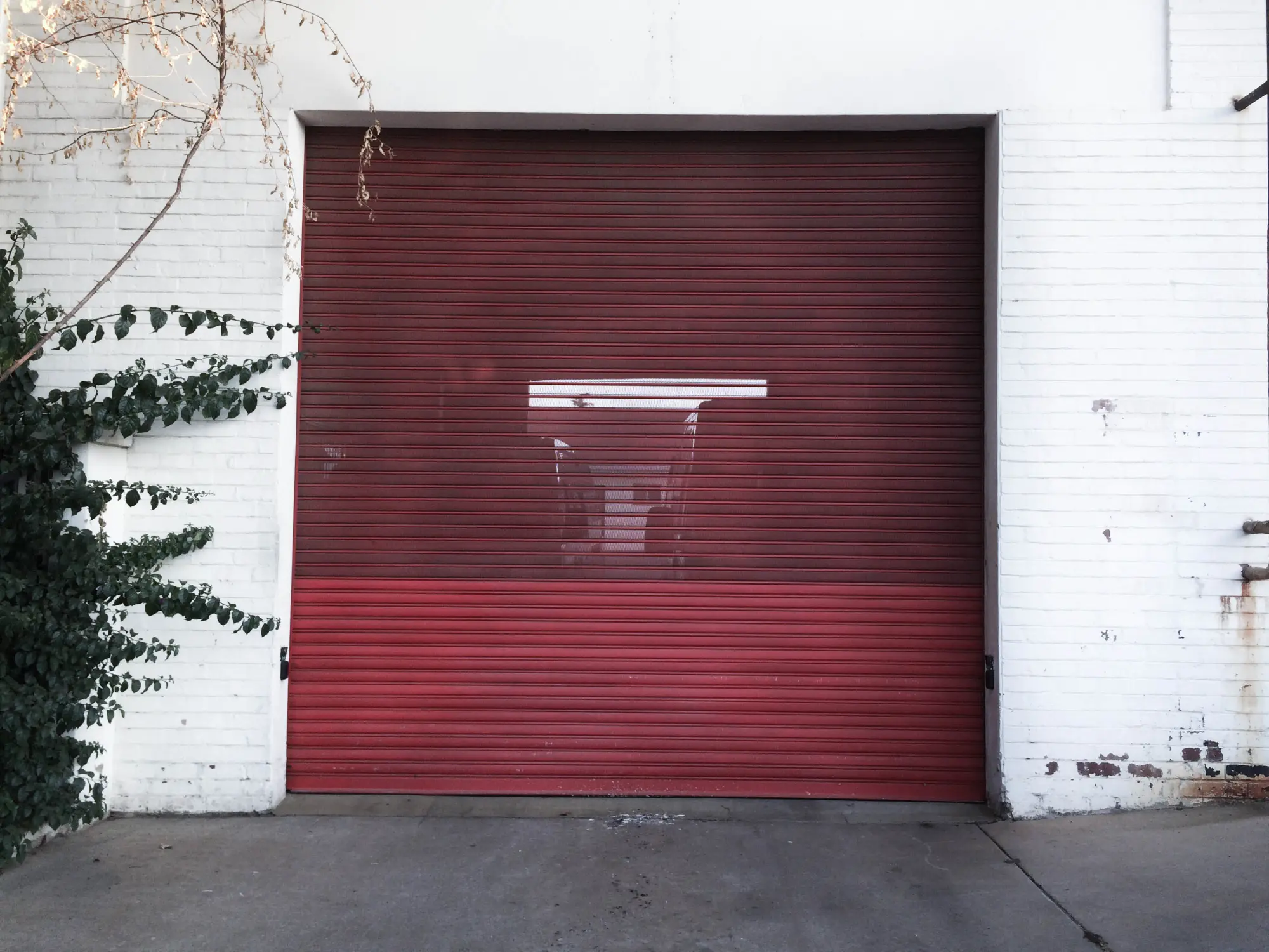 A red rolling garage door on a white brick wall with green ivy.