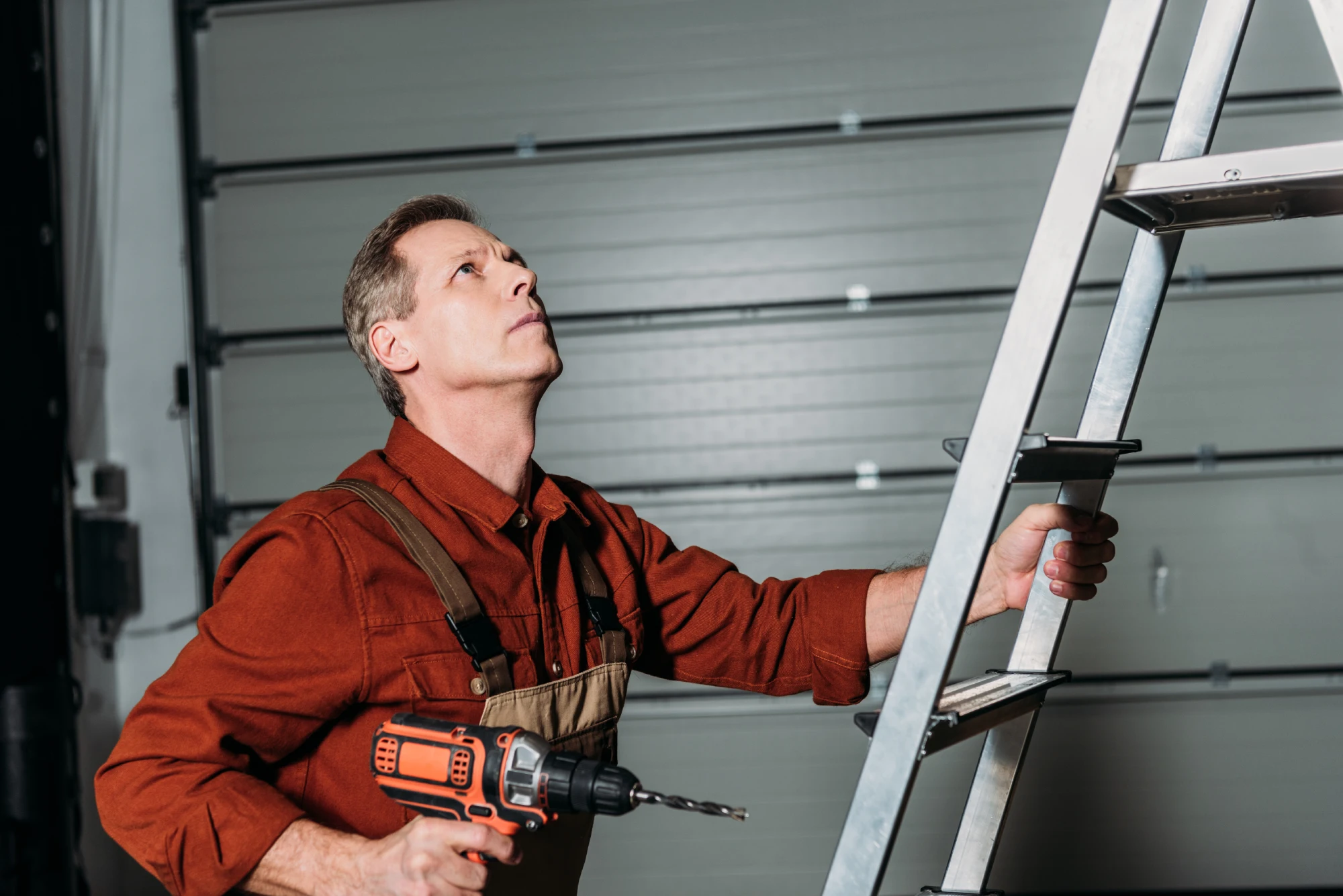 Man in overalls holding a drill and climbing a ladder