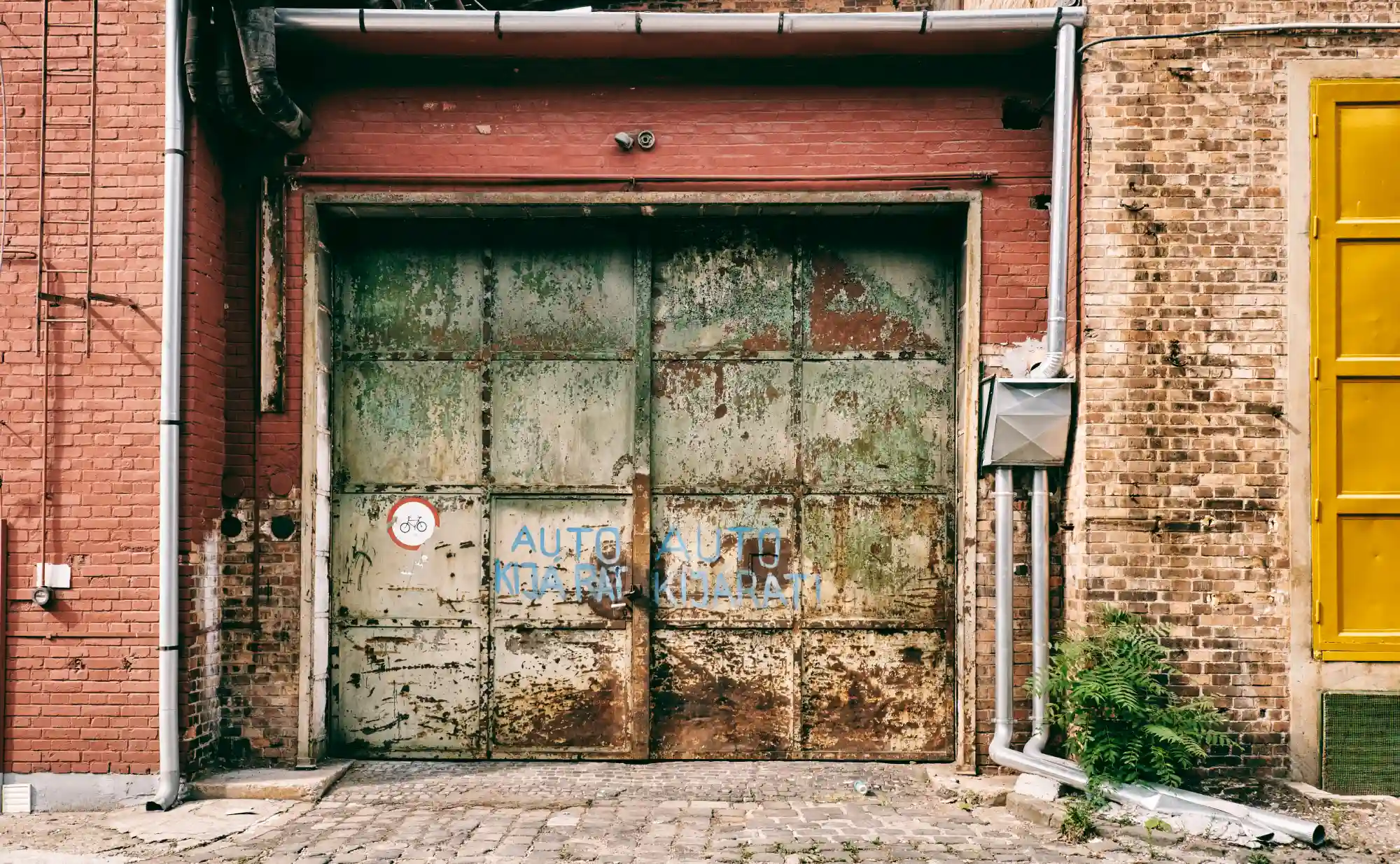 Weathered green metal garage door with graffiti on a brick building
