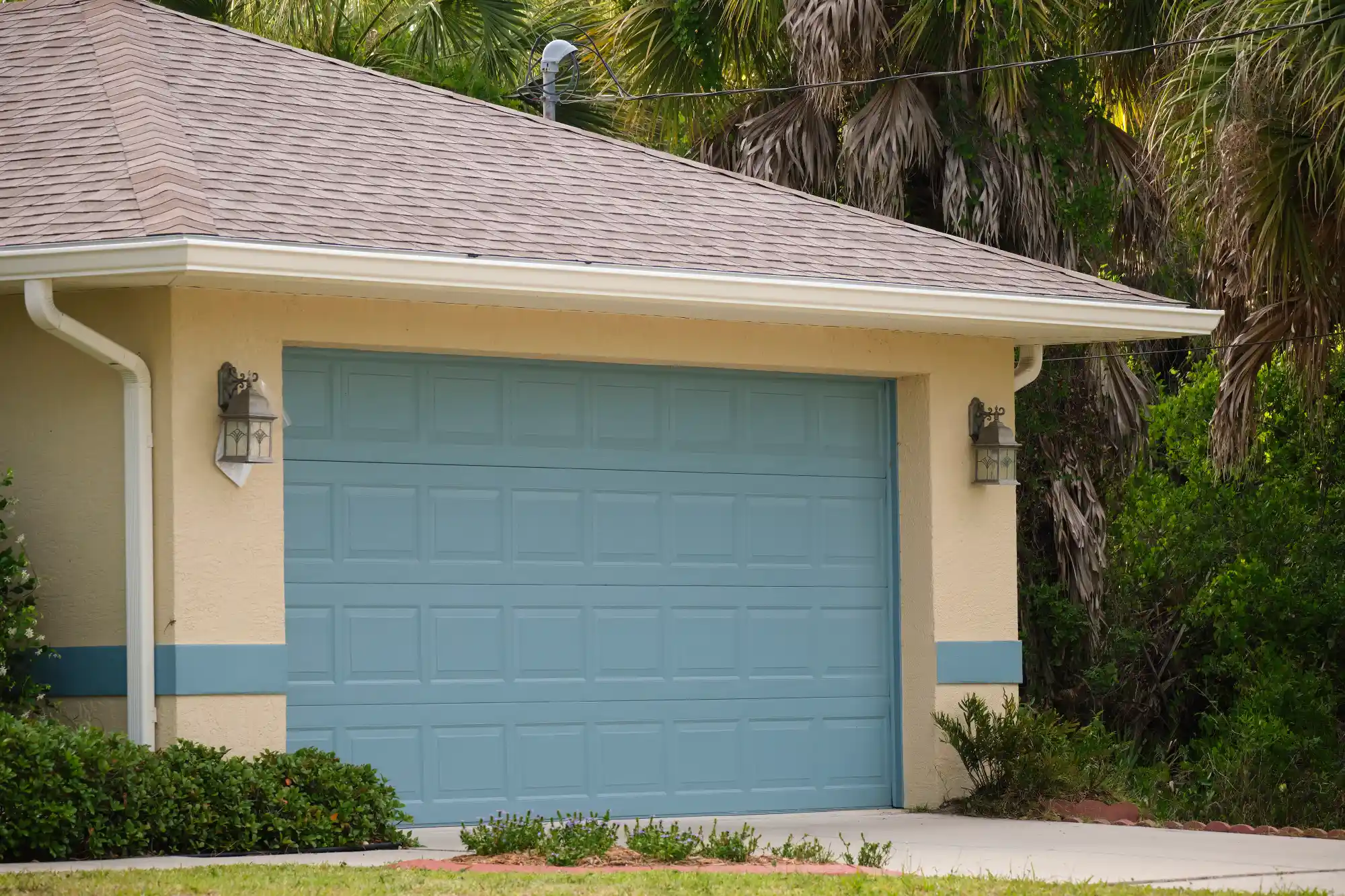 Light blue garage door on a beige house with a brown roof.