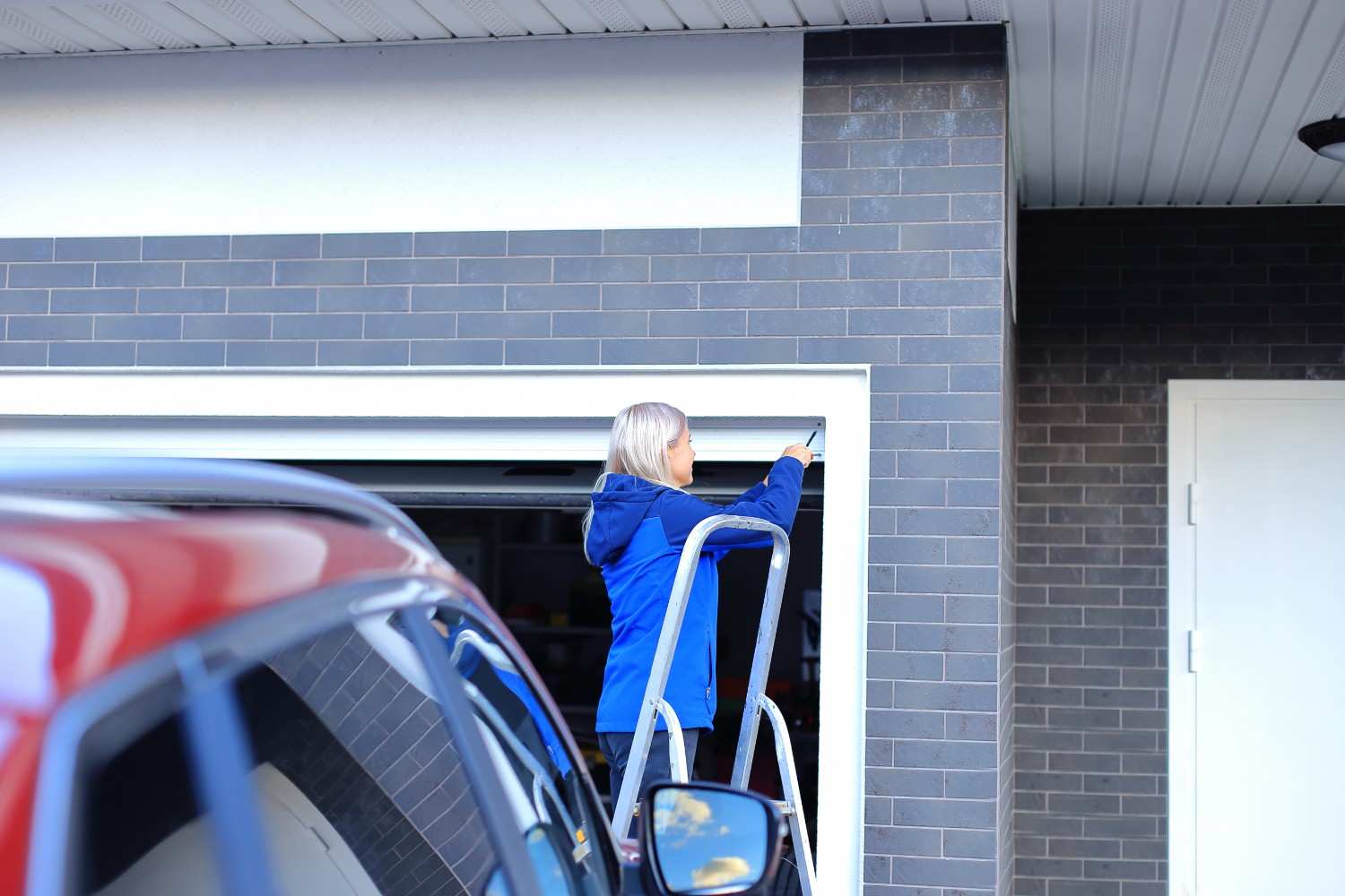 Woman on a ladder working on a garage door frame