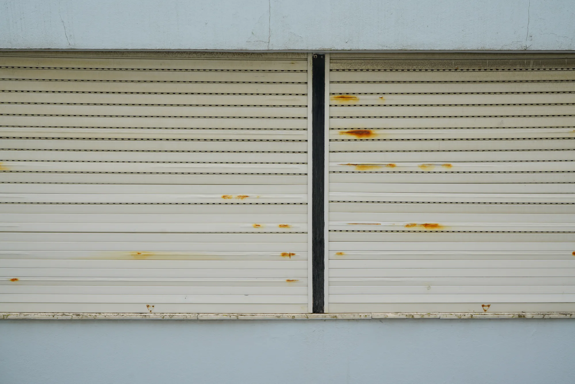 Closed white window shutters with rust stains on a pale blue wall.