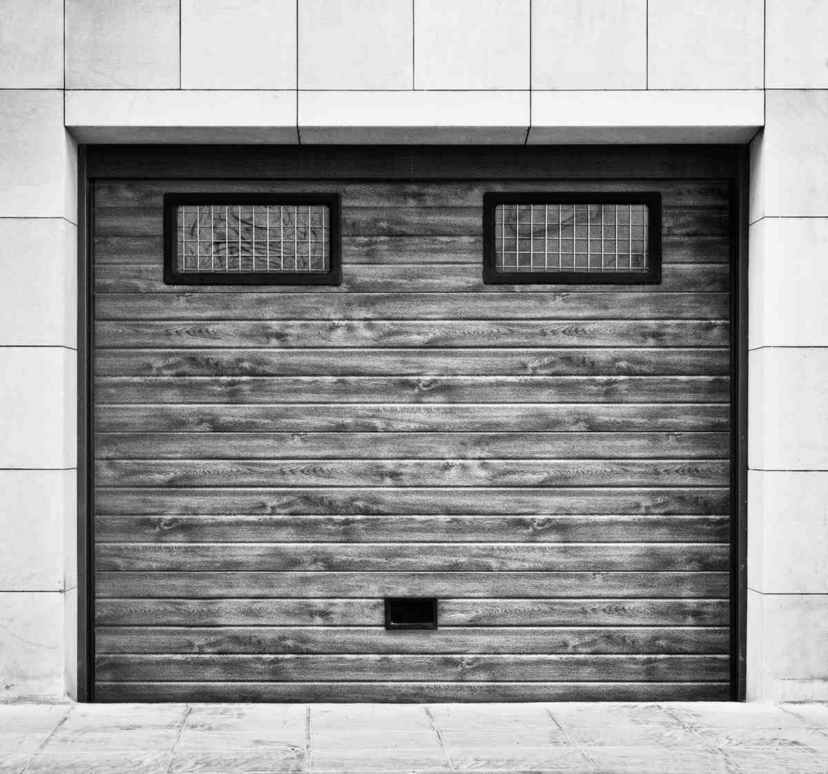 Black and white image of a wooden garage door with two windows and a mail slot.