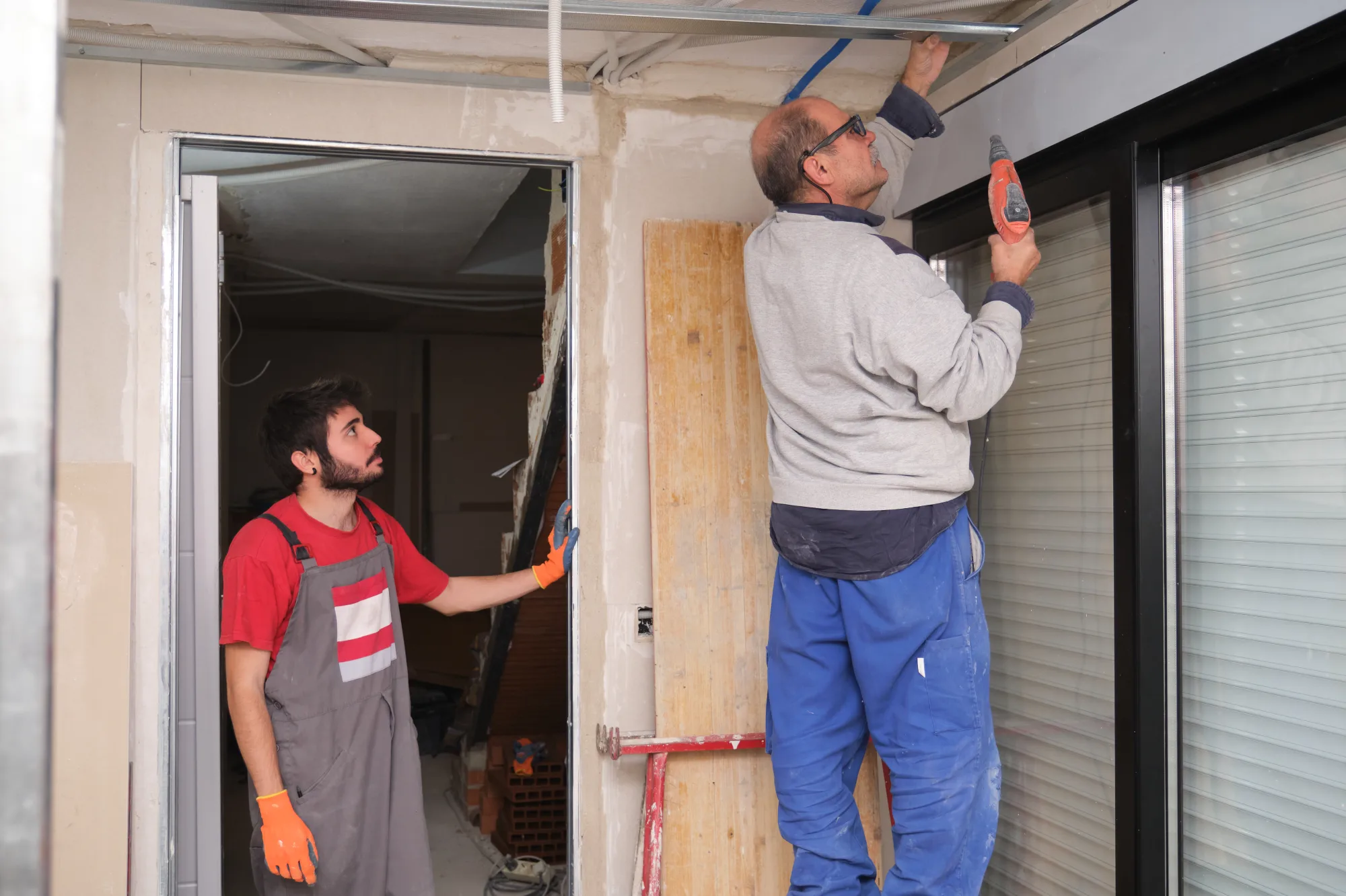 Two men working on a construction site, installing a ceiling and door frame.