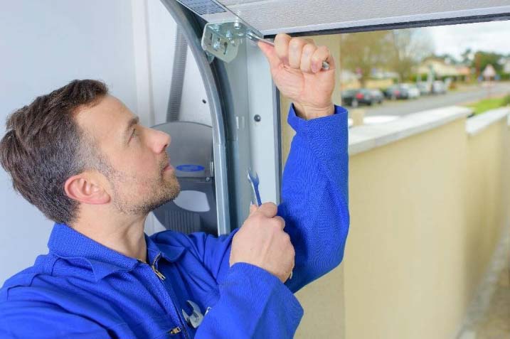 Man in blue overalls repairing a garage door mechanism.