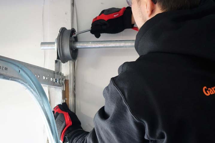 Person wearing safety glasses and gloves working on a garage door spring