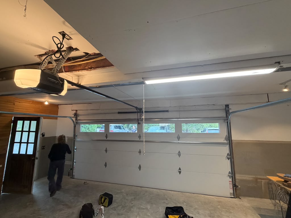 Person walking in a garage with a white garage door and opener.