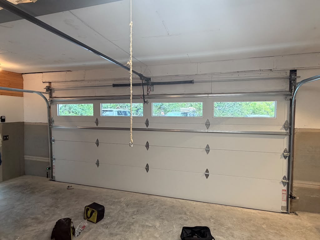 White garage door with windows, partially open, showing exterior trees and vehicles.