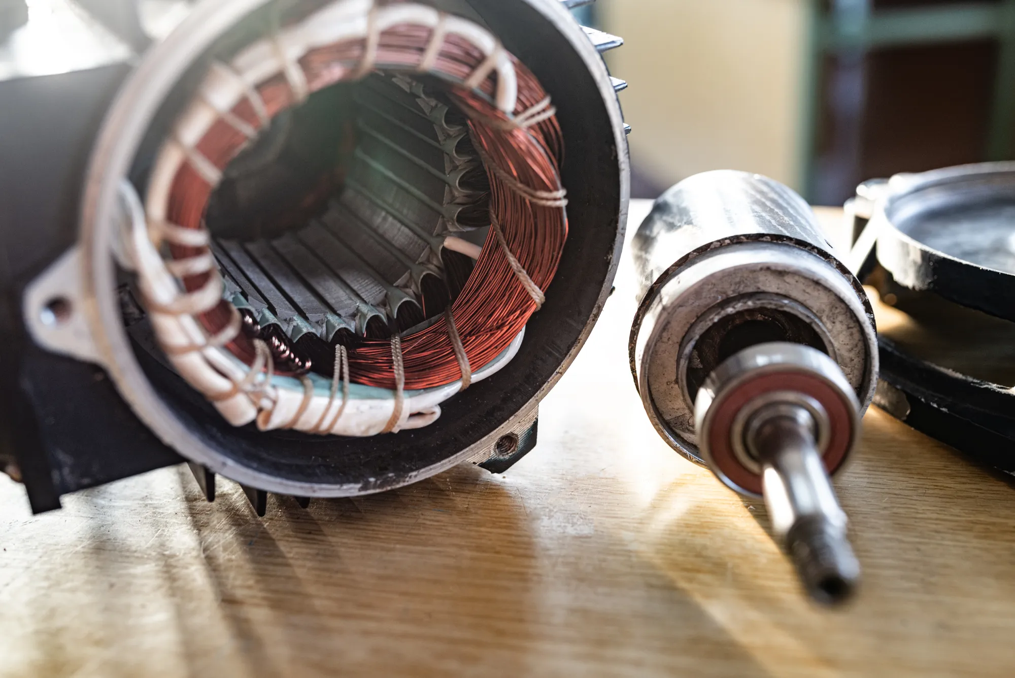 Disassembled electric motor with visible copper windings and rotor on a wooden surface.