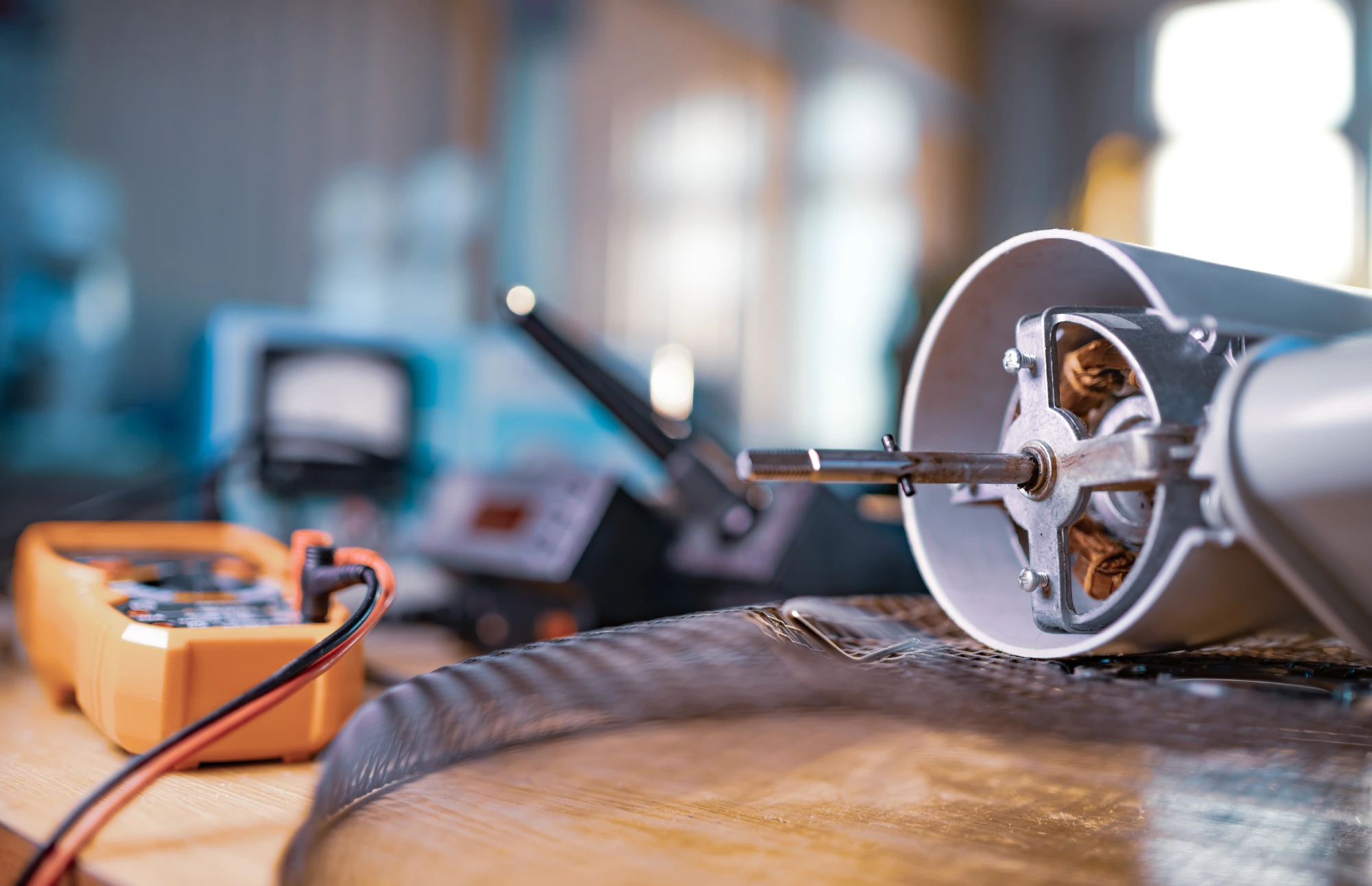 Close-up of a disassembled electric motor and a multimeter on a workbench.