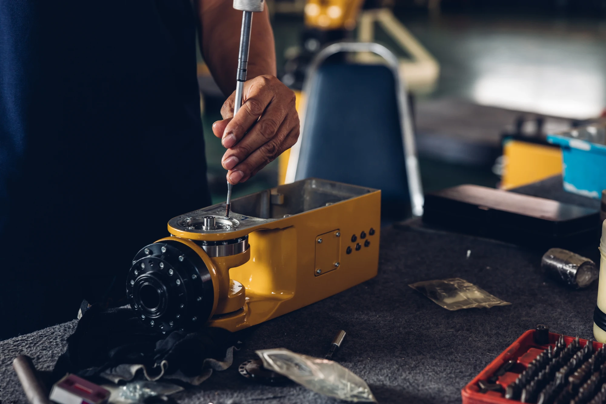 Person using a tool to work on a yellow machine part