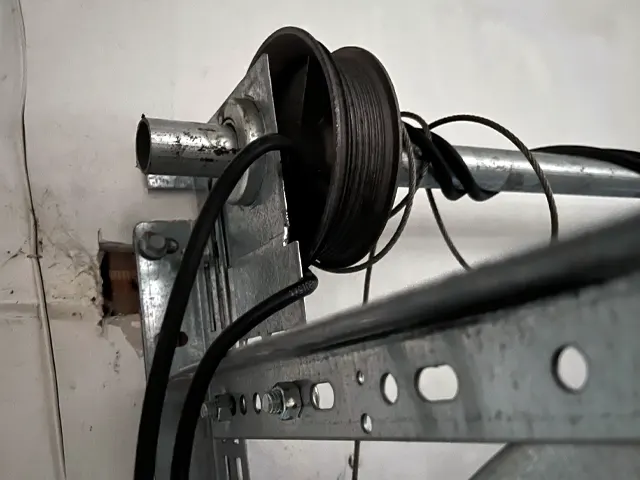 Close-up of a garage door pulley system with wires and metal tracks