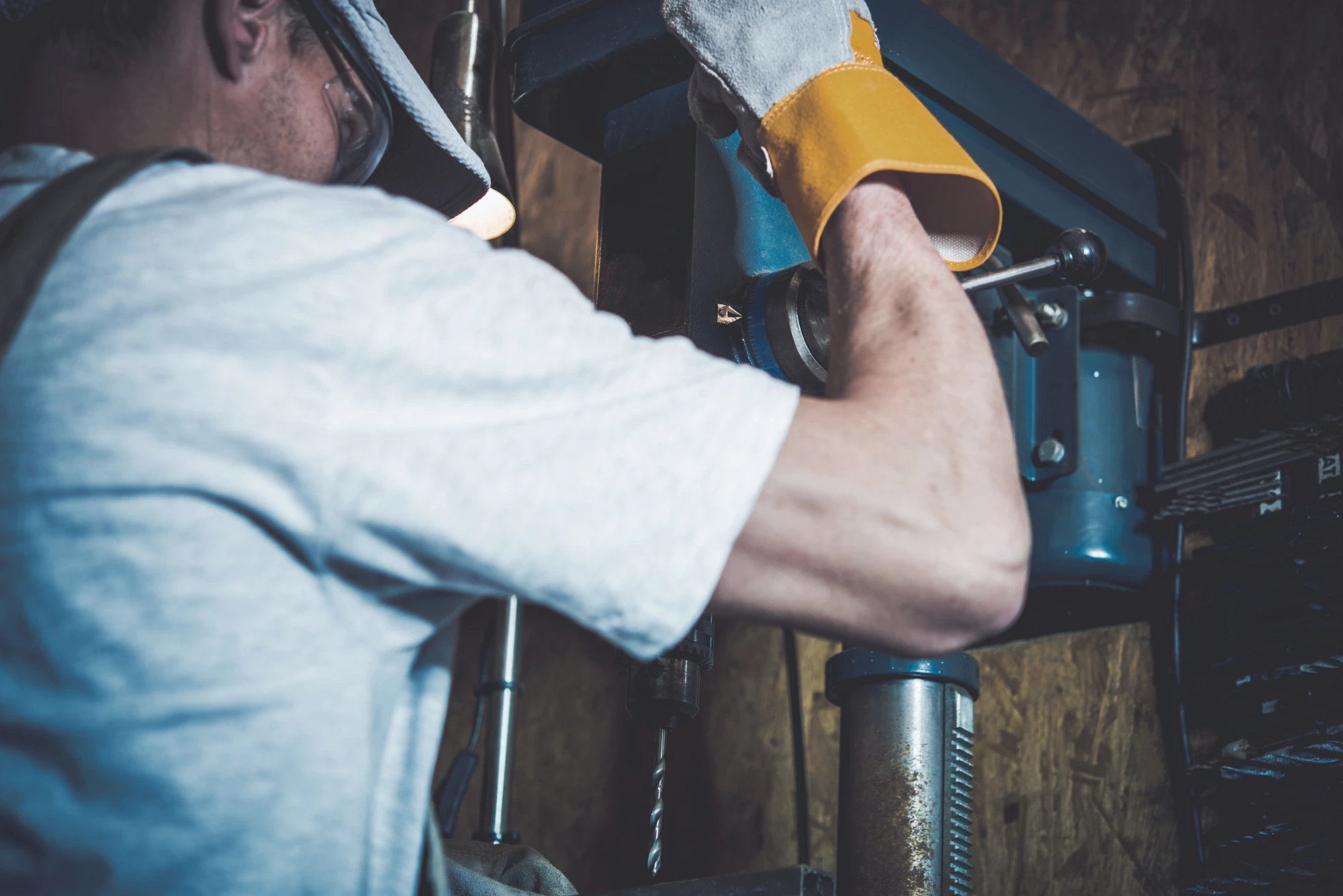 Man in safety glasses and gloves operating a drill press.