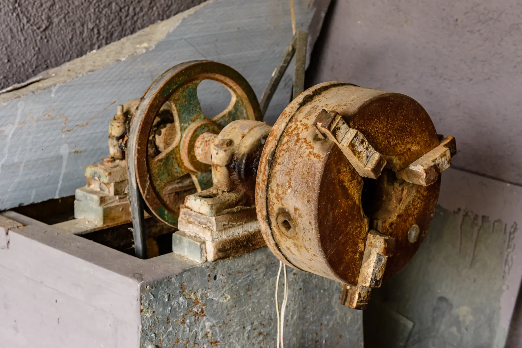 Close-up of a rusty, antique metal lathe machine with a green flywheel.