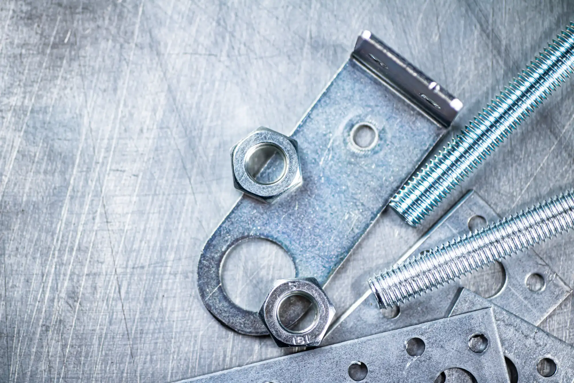 Close-up of metal nuts, bolts, and various hardware pieces on a scratched surface.