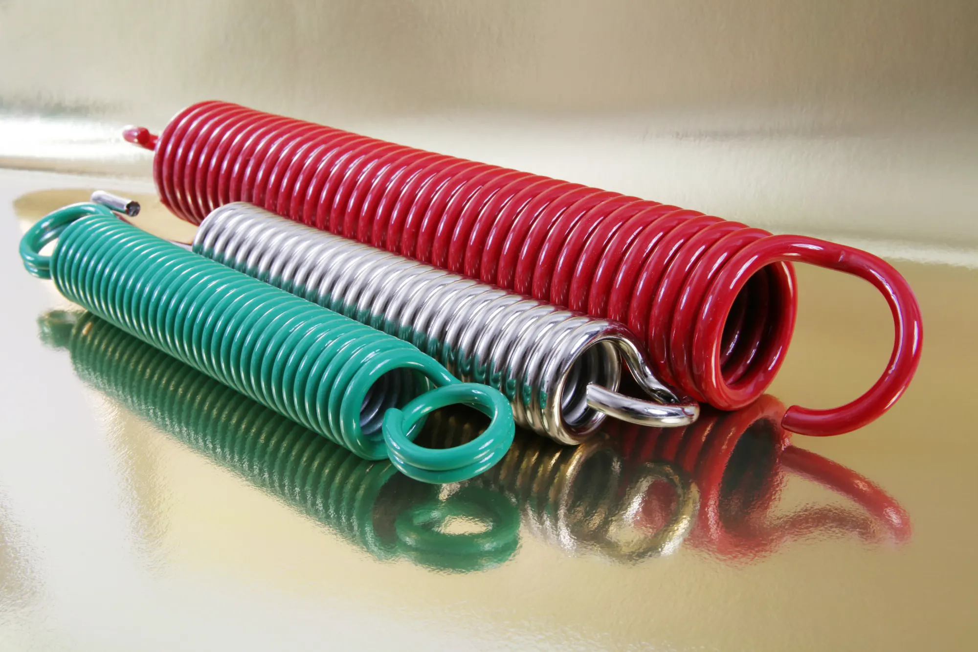 Three industrial springs: red, silver, and green, on a golden surface.
