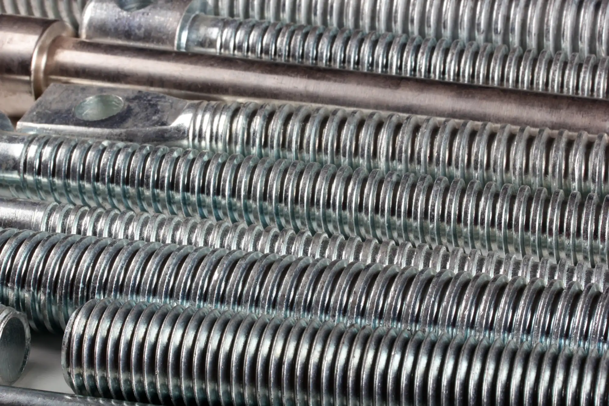 Close-up of numerous shiny, silver-colored threaded rods and bolts.