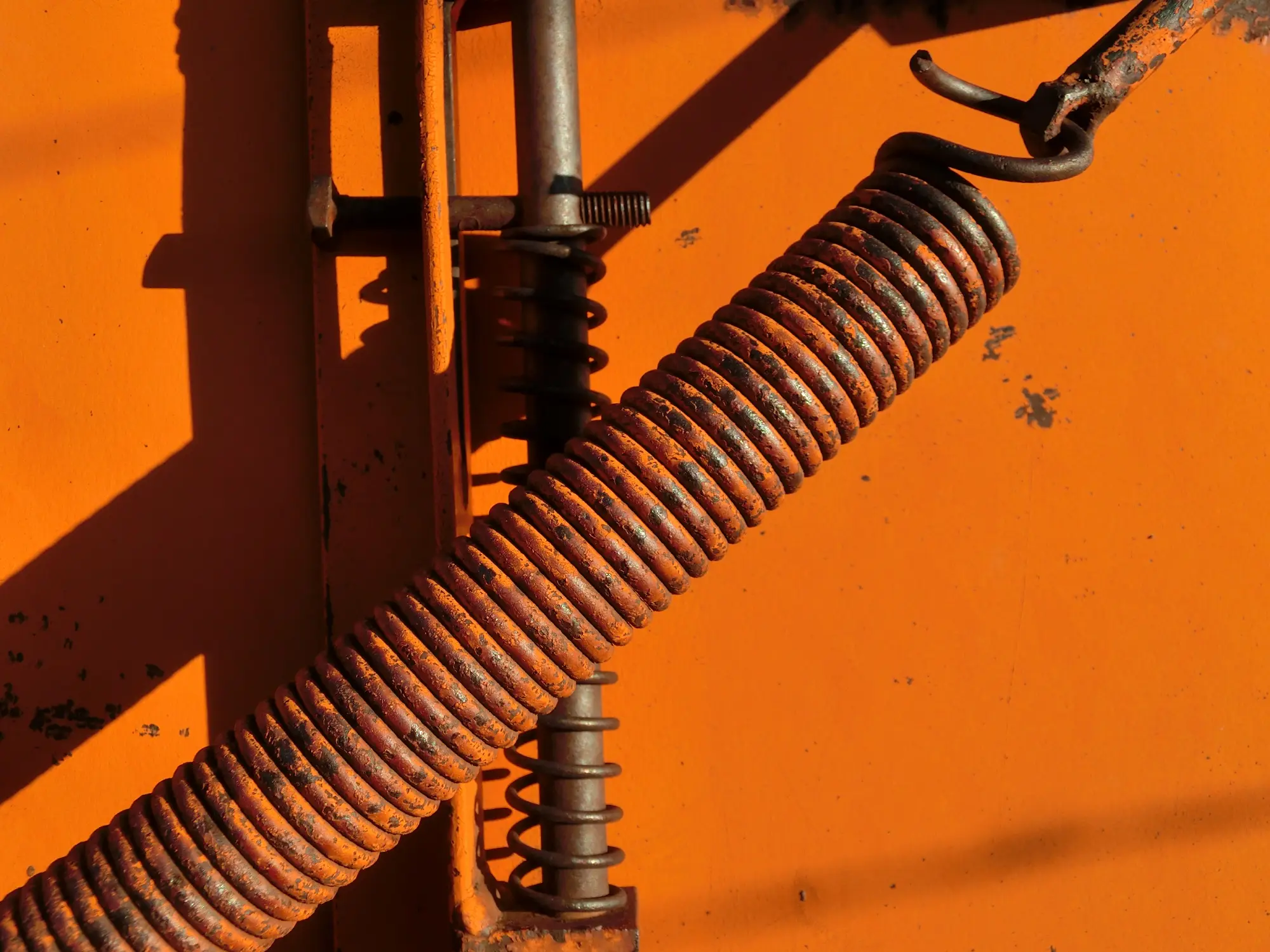 Close-up of a rusty metal spring against a bright orange background.