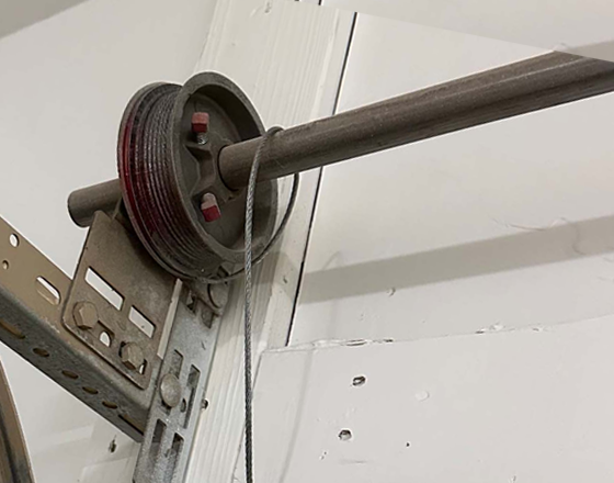 Close-up of a garage door pulley system with a cable and shaft.
