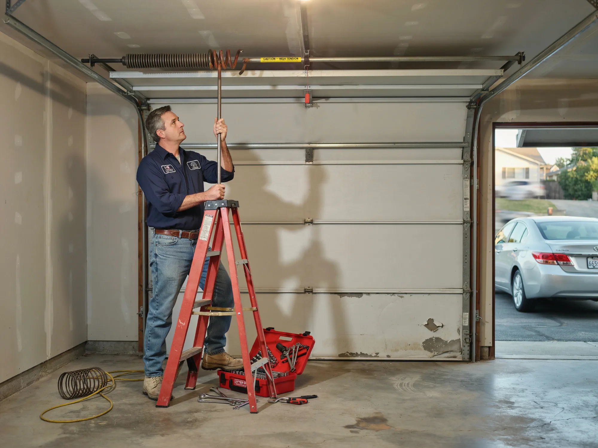 Man on a ladder repairing a garage door spring system.