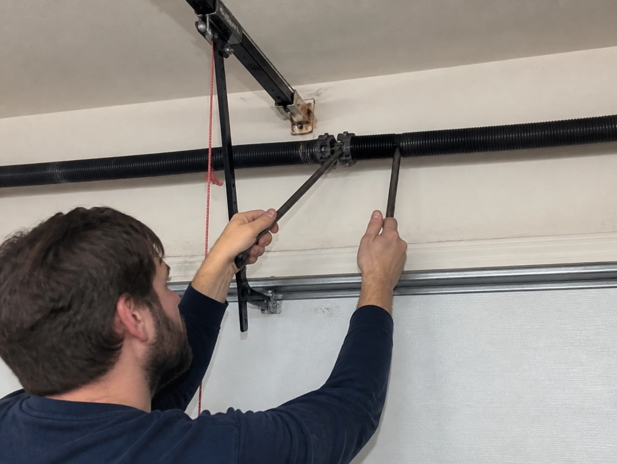 Man adjusting a garage door torsion spring with two winding bars.